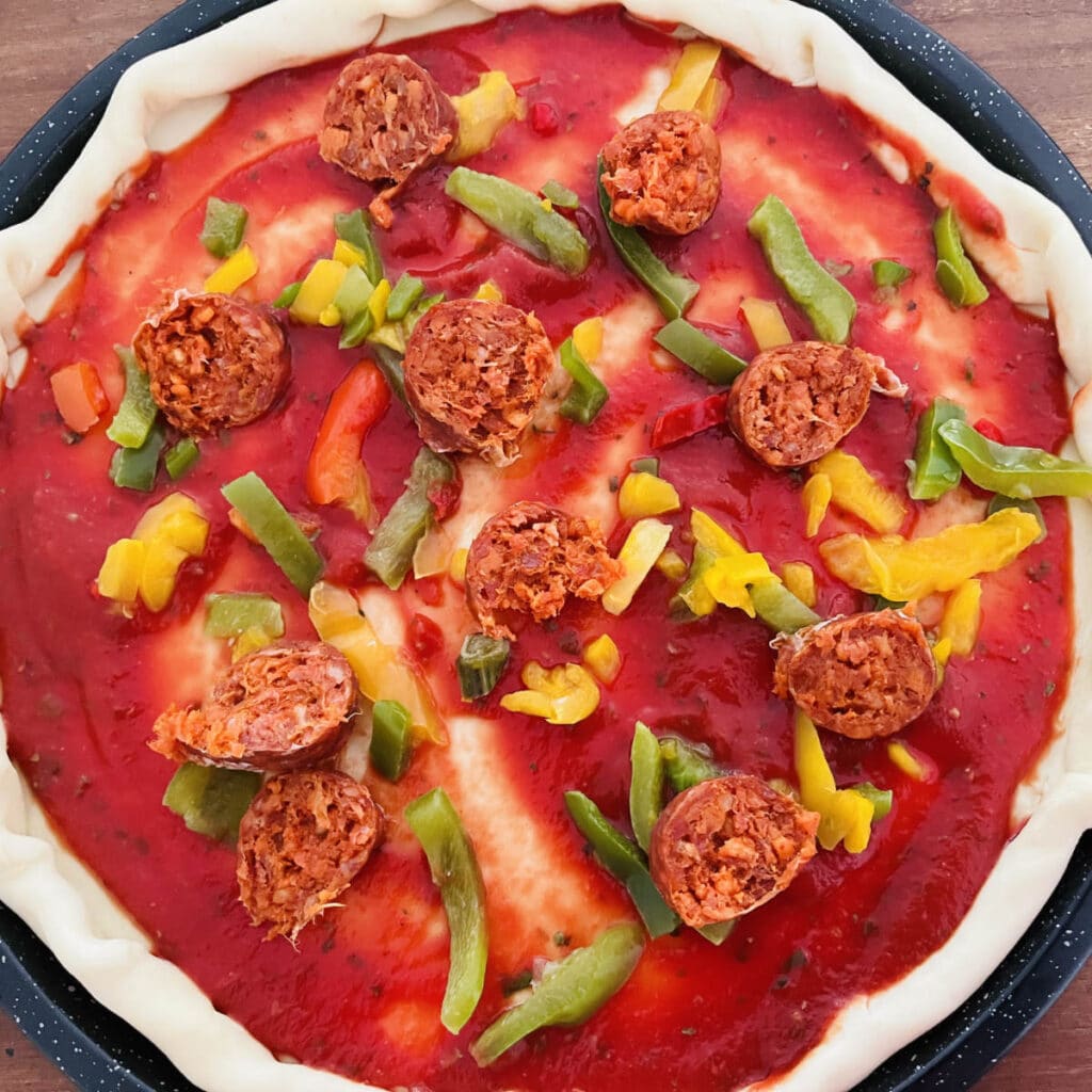 chorizo and red, green, and yellow peppers on a pizza base with tomato sauce.