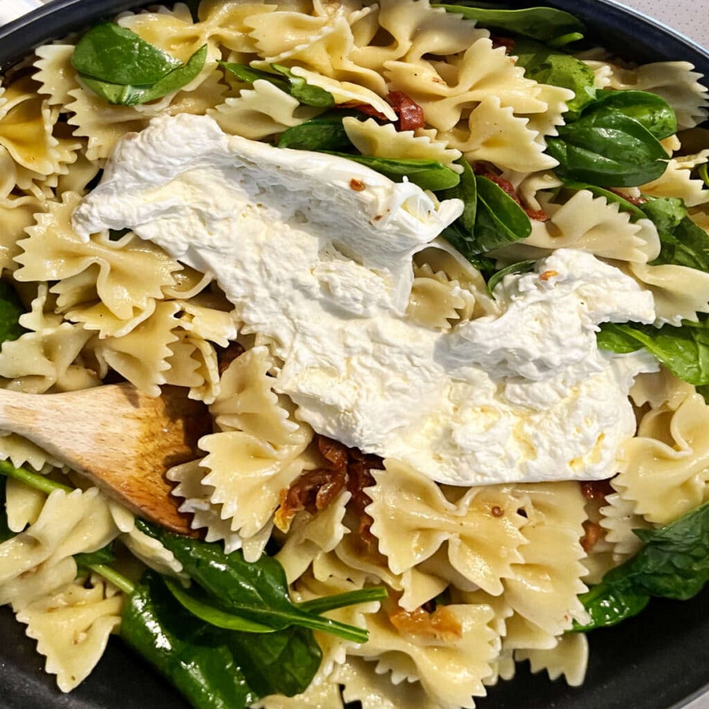 Burrata added into the pasta with spinach and sun-dried tomatoes on a stove top