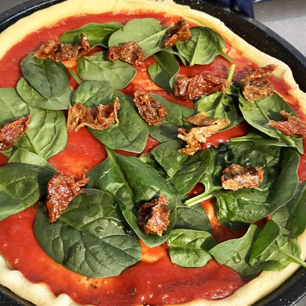 sun-dried tomatoes on bed of spinach on a pizza with tomato sauce