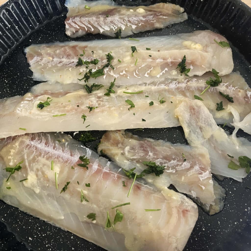 uncooked tilapia in a pan, ready for the oven
