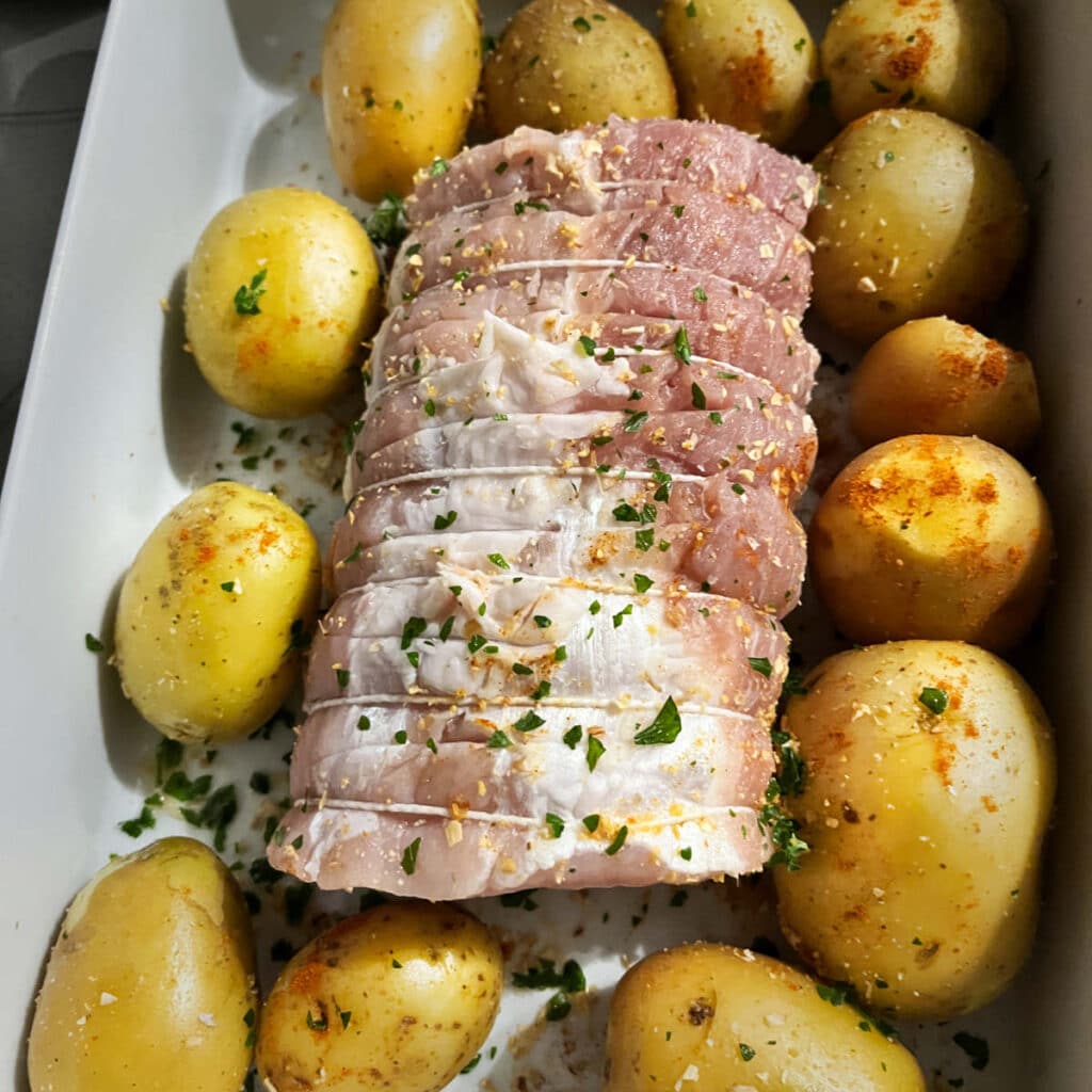 Pork loin and potatoes covered in herbs and spices, ready for the oven